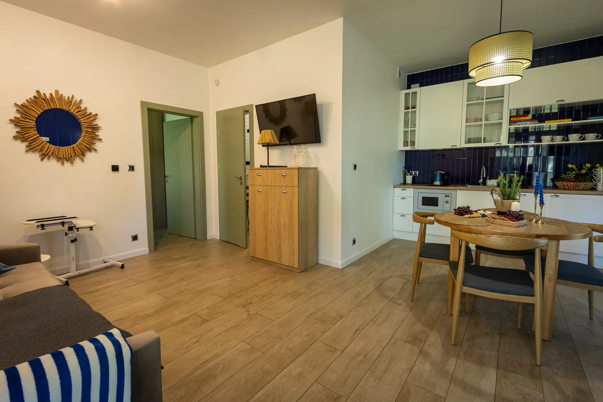 Salon z jadalnią i aneksem kuchennym — złote lustro słoneczne, telewizor i granatowa ściana kuchni — Apartament 3 Poezja Ciszy Dębki